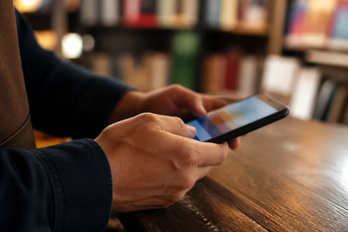 Mains d&rsquo;un commerçant consultant un smartphone au-dessus du comptoir en bois d&rsquo;une librairie