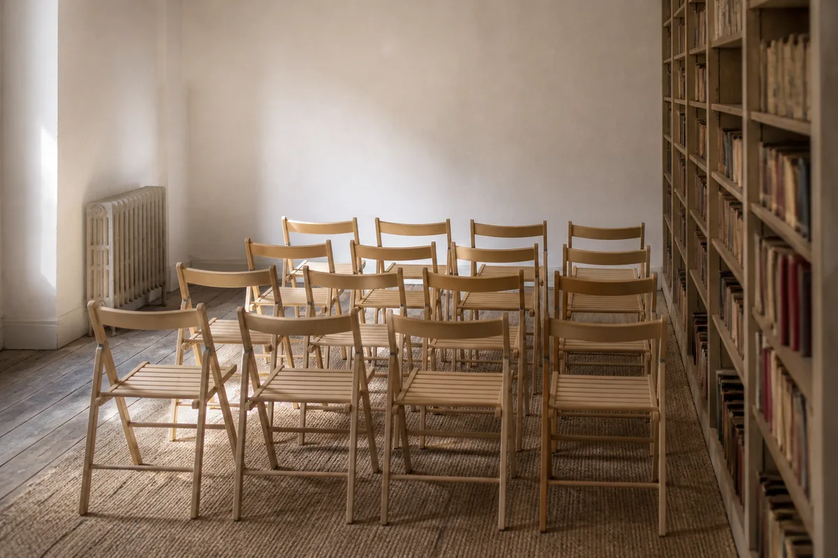Rangée de chaises en bois alignées dans une petite salle aux murs clairs