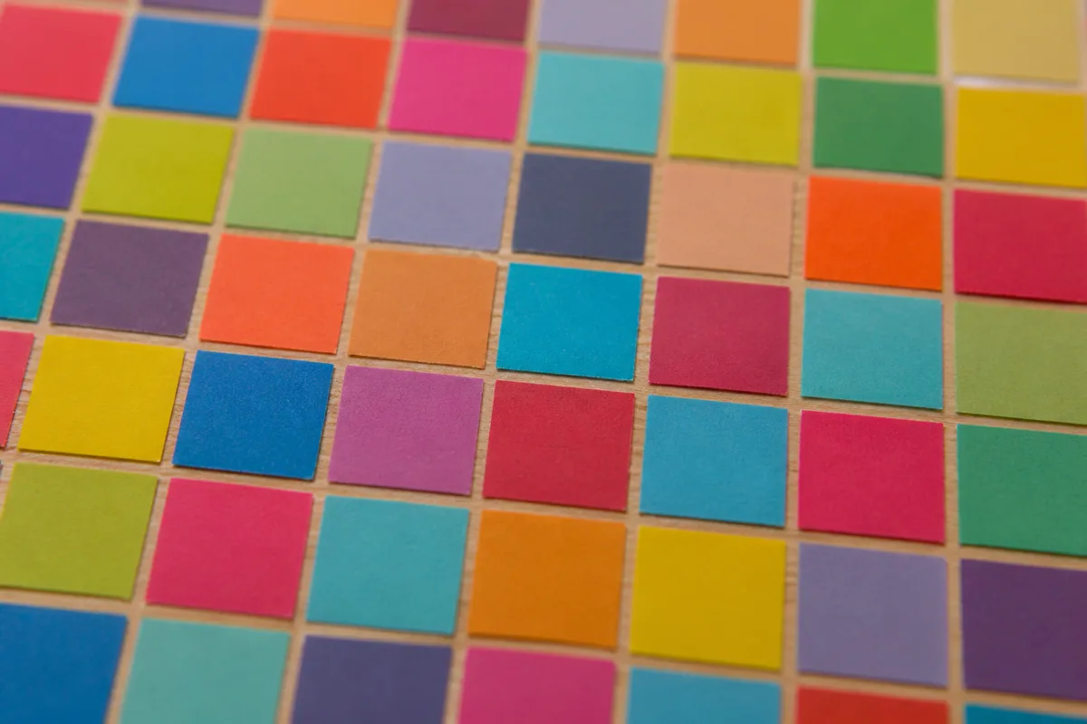 Mosaïque de petits carrés de papier coloré collés côte à côte sur un panneau de bois clair